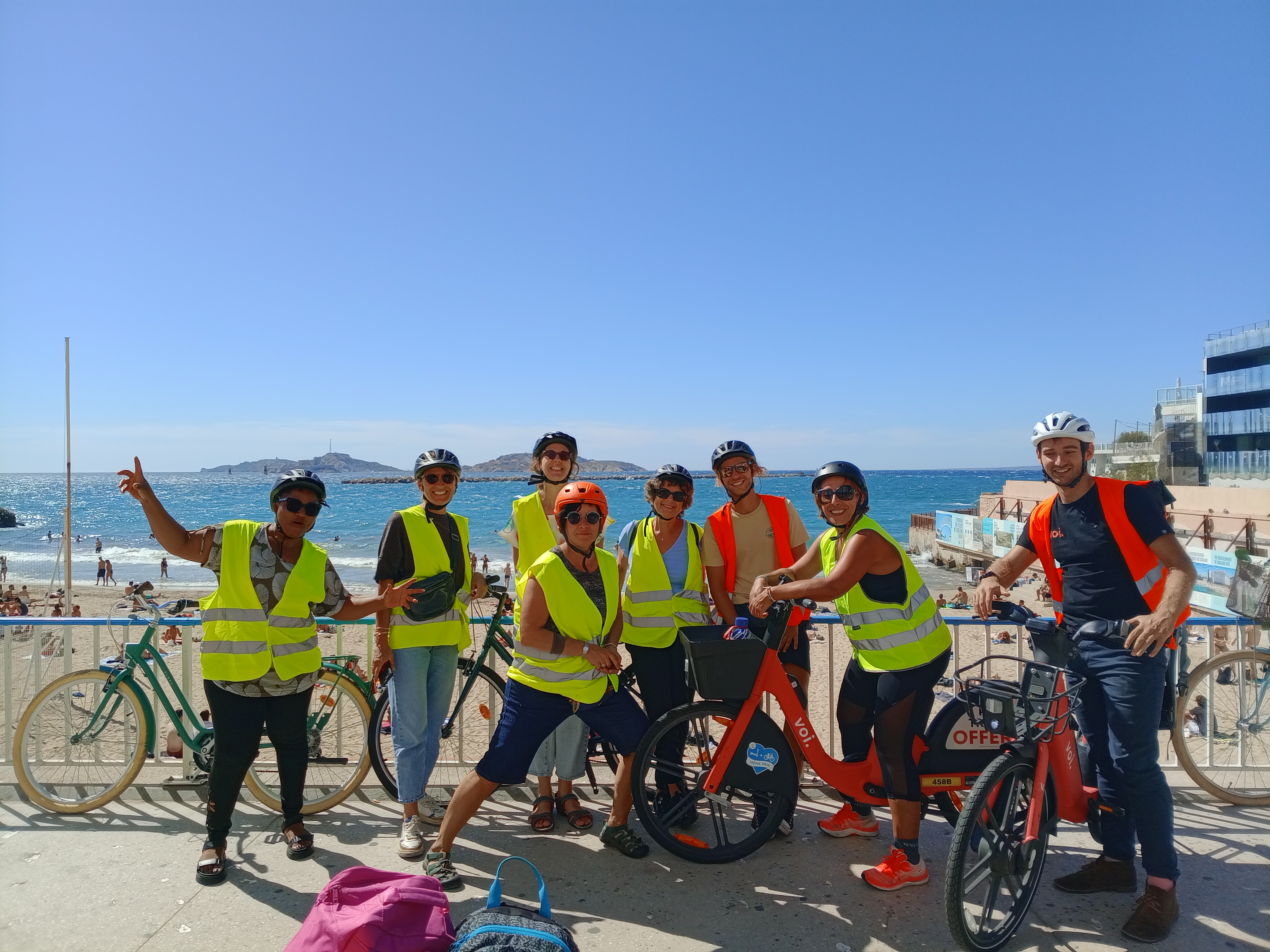Image 1 : Groupe de cyclistes portant des gilets de sécurité sur le bord de mer à Marseille, avec les îles du Frioul en arrière-plan.